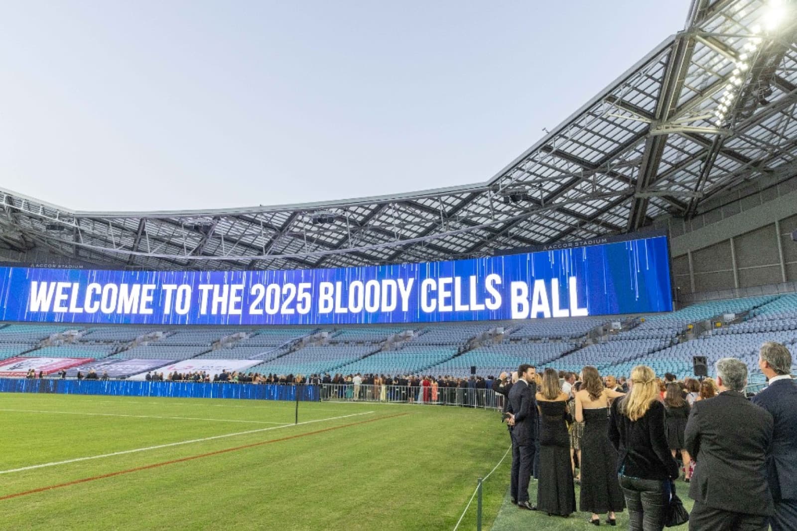 The full dining room of the 2025 Bloody Cells Ball with guests seated and the event wordmark glowing in the background