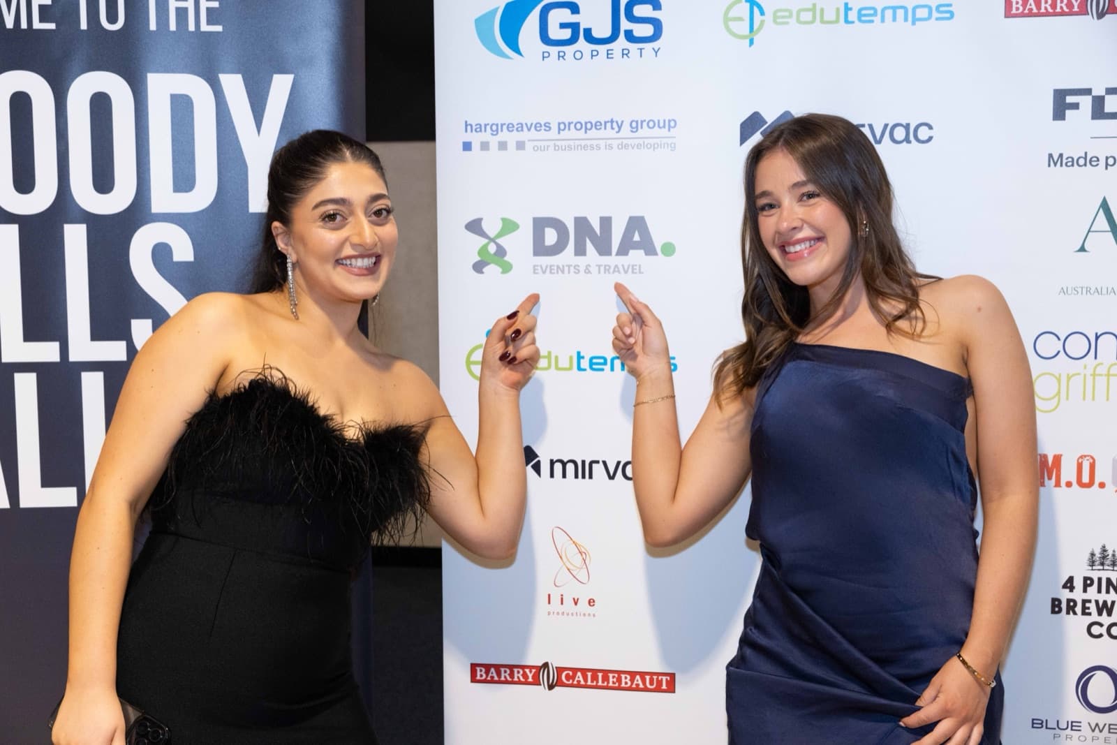 Two sponsor guests pointing out their family business logo on the 2025 Bloody Cells Ball sponsor wall