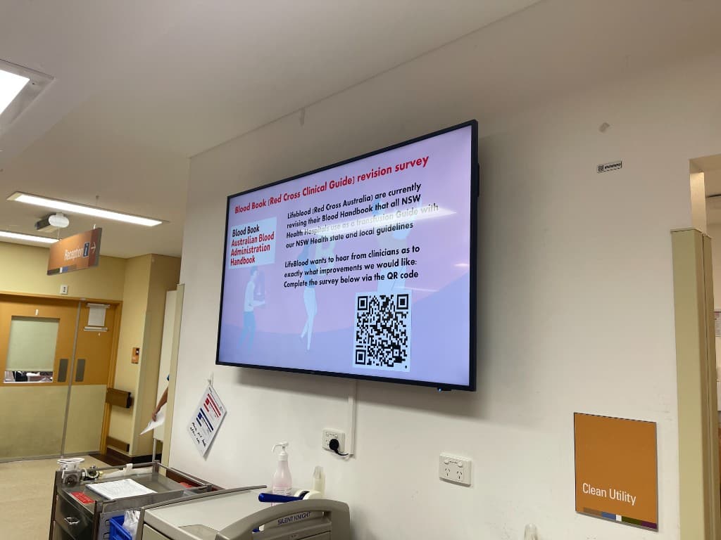 A new ward screen near the Clean Utility area displaying the Lifeblood / Australian Blood Administration Handbook (Blood Book) revision survey for clinicians, with a QR code to complete the survey
