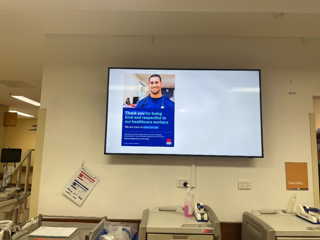 A new ward screen near the Clean Utility area showing the NSW Health 'Thank you for being kind and respectful to our healthcare workers' staff-care campaign